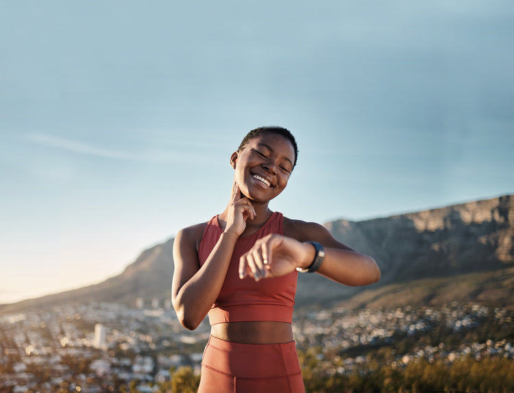 A woman in athletic clothing smiling and checking her pulse with her finger.