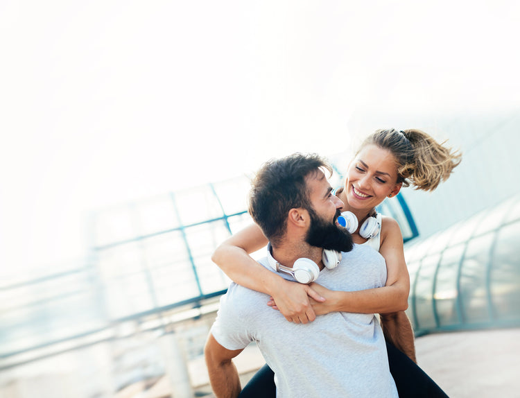 A woman piggybacking on a man. They are looking at each other and smiling.