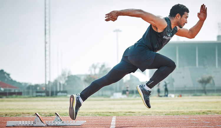 A man in black athletic attire, beginning to run on an outdoor track.