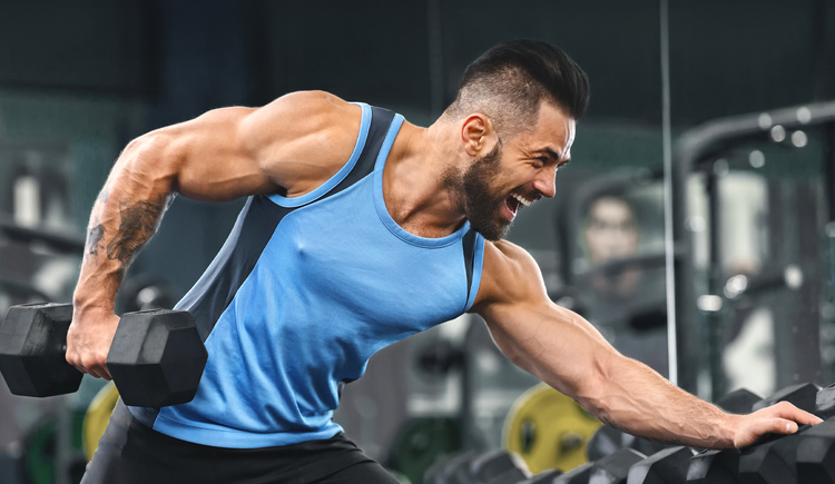 A man with large muscles lifting weights at the gym, with his mouth open and eyes squinting.