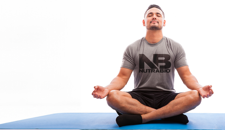 Man wearing a NutraBio Brands T-shirt, meditating cross-legged on a blue yoga mat.