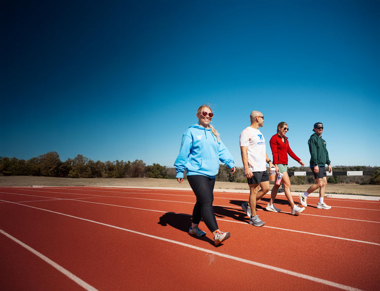 Two women and two men, all wearing sunglasses while they walk on an outdoor track on an autumn day.