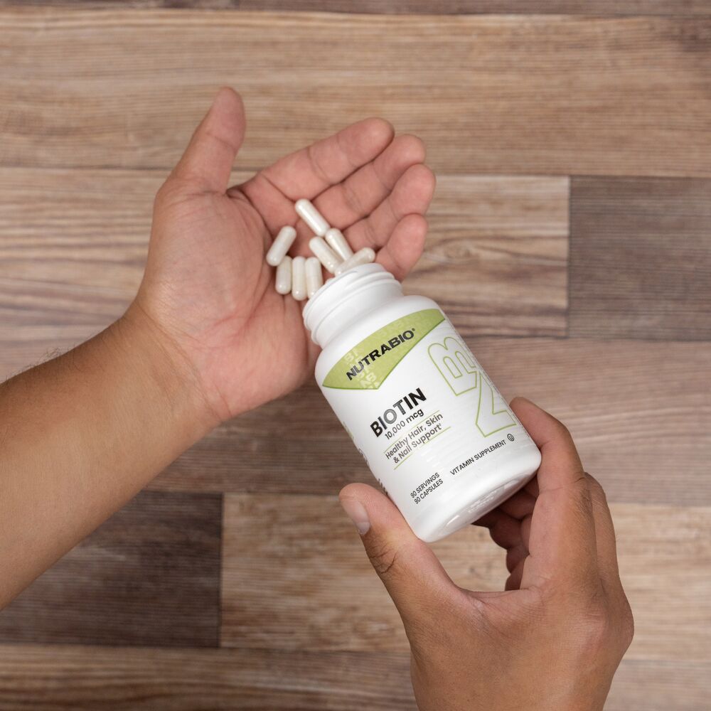 Person holding a bottle of NutraBio Biotin with capsules on a wooden surface