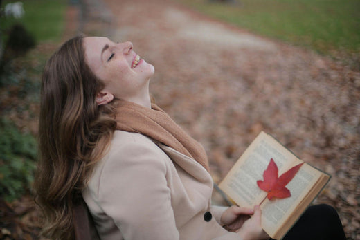 Caucasian woman sitting in the park on an autumn day, laughing with a book in her hands.