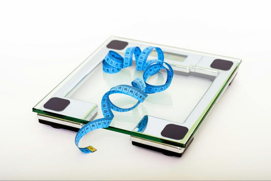 A glass digital bathroom scale with a blue measuring tape coiled on top.
