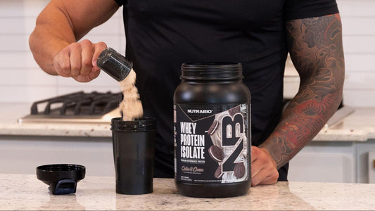 A person is seen pouring NutraBio Whey Protein Isolate into a shaker cup in a kitchen setting