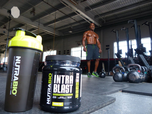 One NutraBio shaker cup and a bottle Intra Blast on a gym floor with a shirtless athletic man in the background.