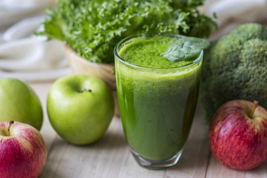 Apples and kale sitting on a table next to a green smotthie in a glass