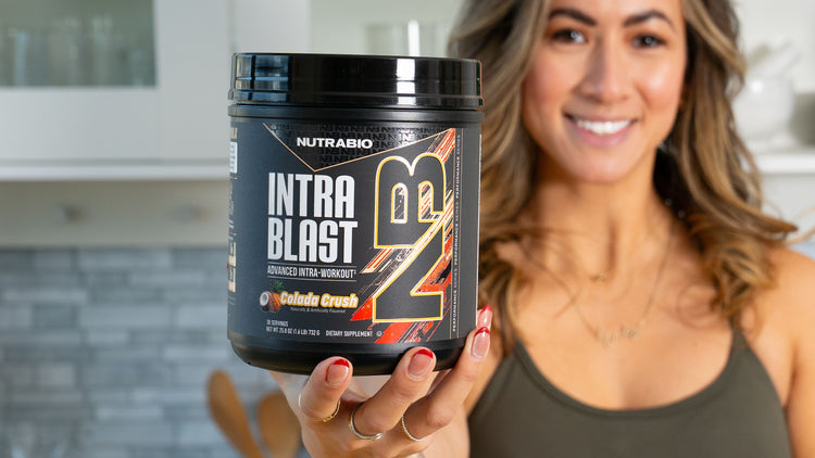 Woman holding a NutraBio Intra Blast supplement container in a kitchen setting