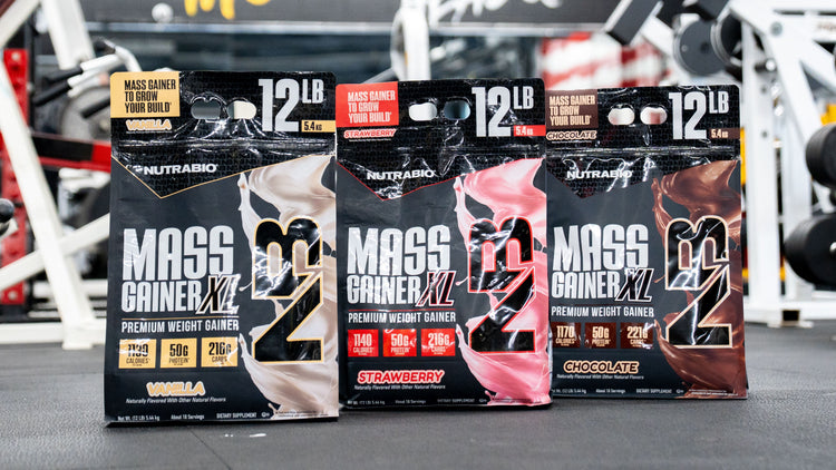 Three packages of NutraBio Mass Gainer XL in different flavors on a gym floor.