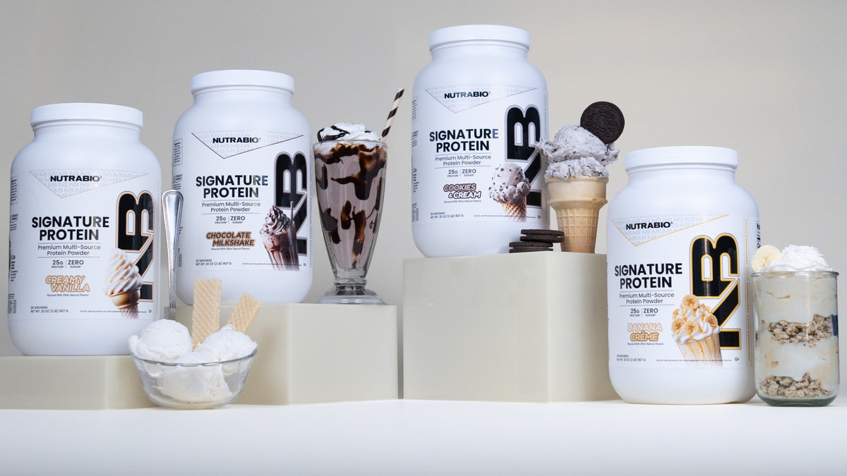 Three tubs of Nutrabio Signature Protein powder in Creamy Vanilla, Chocolate Milkshake, Cookies & Cream, and Banana Crème flavors, displayed alongside a milkshake, ice cream, and a yogurt parfait.