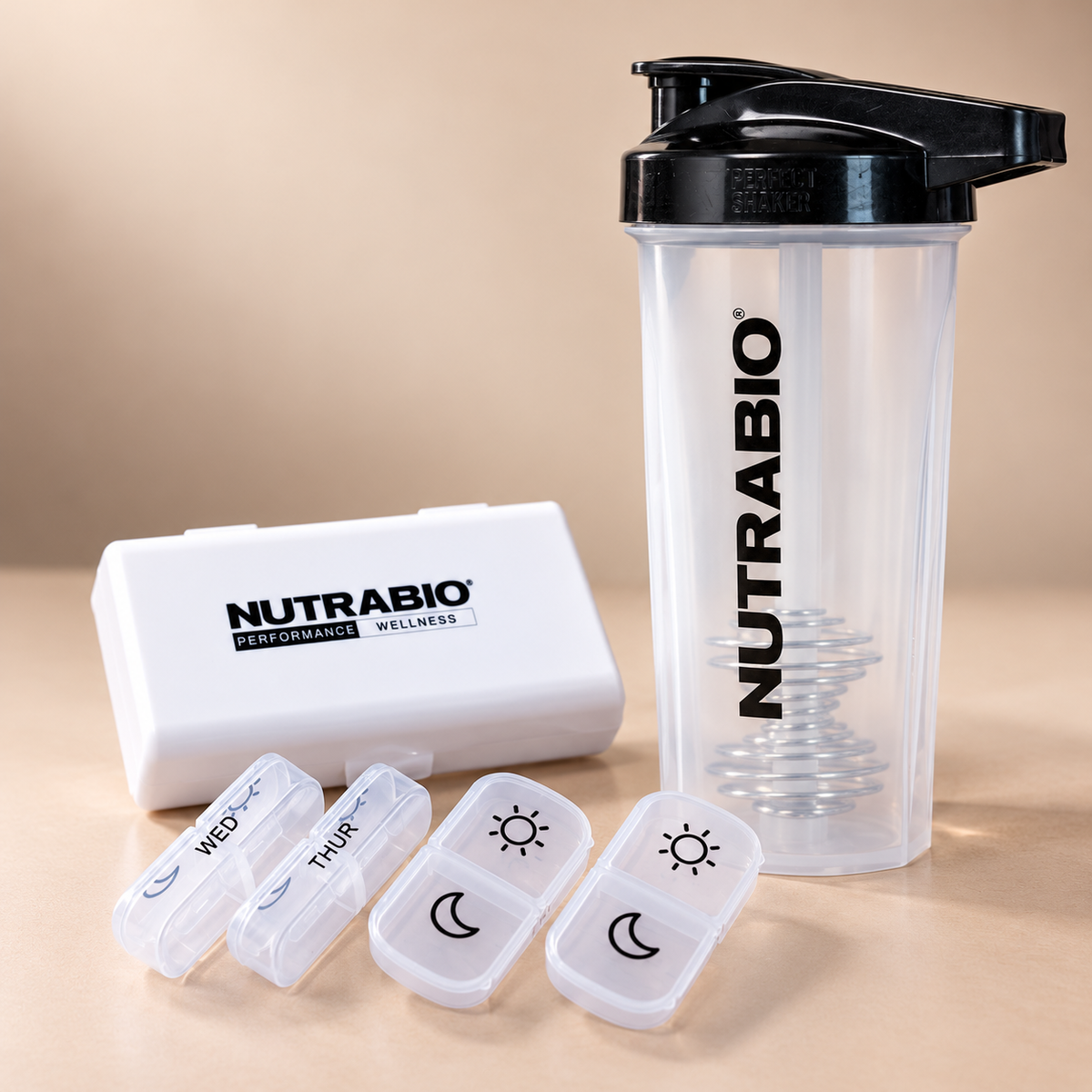 A Daily Routine Kit featuring a clear protein shaker bottle with a wire whisk ball next to a white pill organizer with four small daily compartments labeled with sun and moon icons.