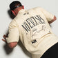 Person wearing a beige no excuses shirt with text and logos on a plain background