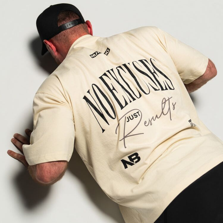 Person wearing a beige no excuses shirt with text and logos on a plain background